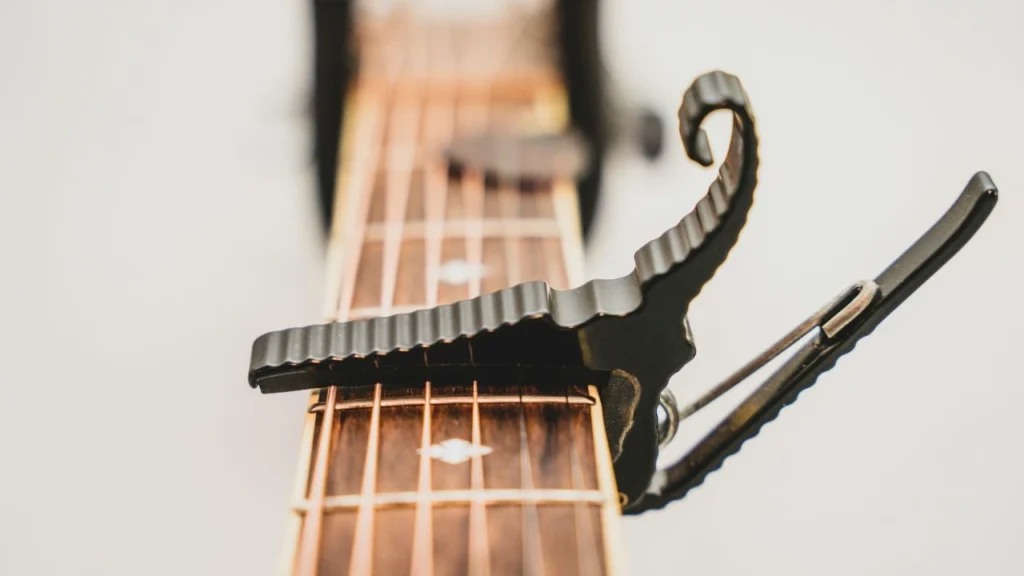 Close-up top view of a black metal trigger capo attached to a rosewood guitar fretboard