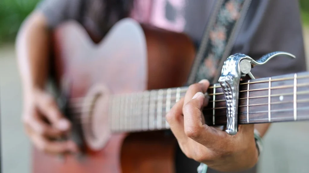 Musician playing an acoustic guitar with a silver crocodile-shaped capo clamped on the fretboard